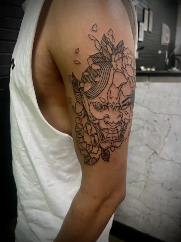 Detailed black ink mask tattoo on an upper arm